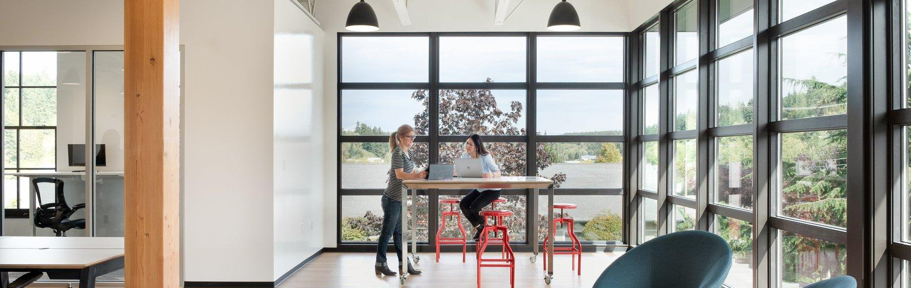 two women with laptops at high top table in modern office building space