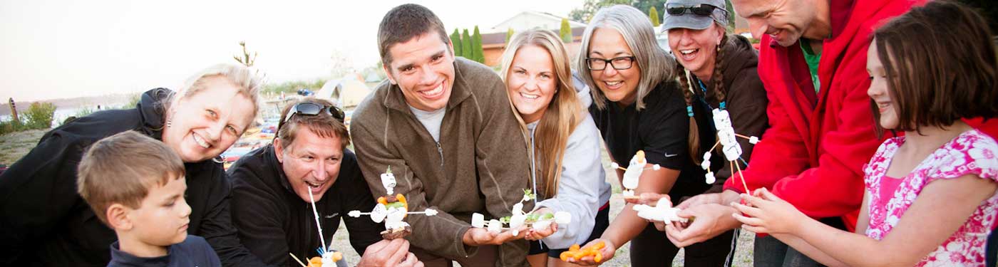 group of smiling people with marshmallow figures on roasting sticks