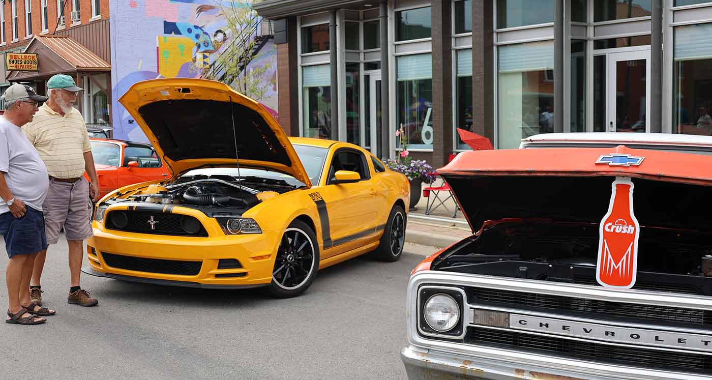 car show downtown, two men looking under the hood of a Ford Mustang