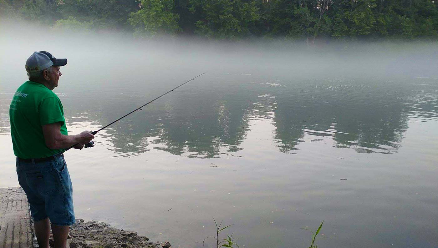 Man fishing on the shore of a foggy river
