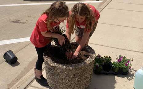 Children planting flowers in a large pot on main street