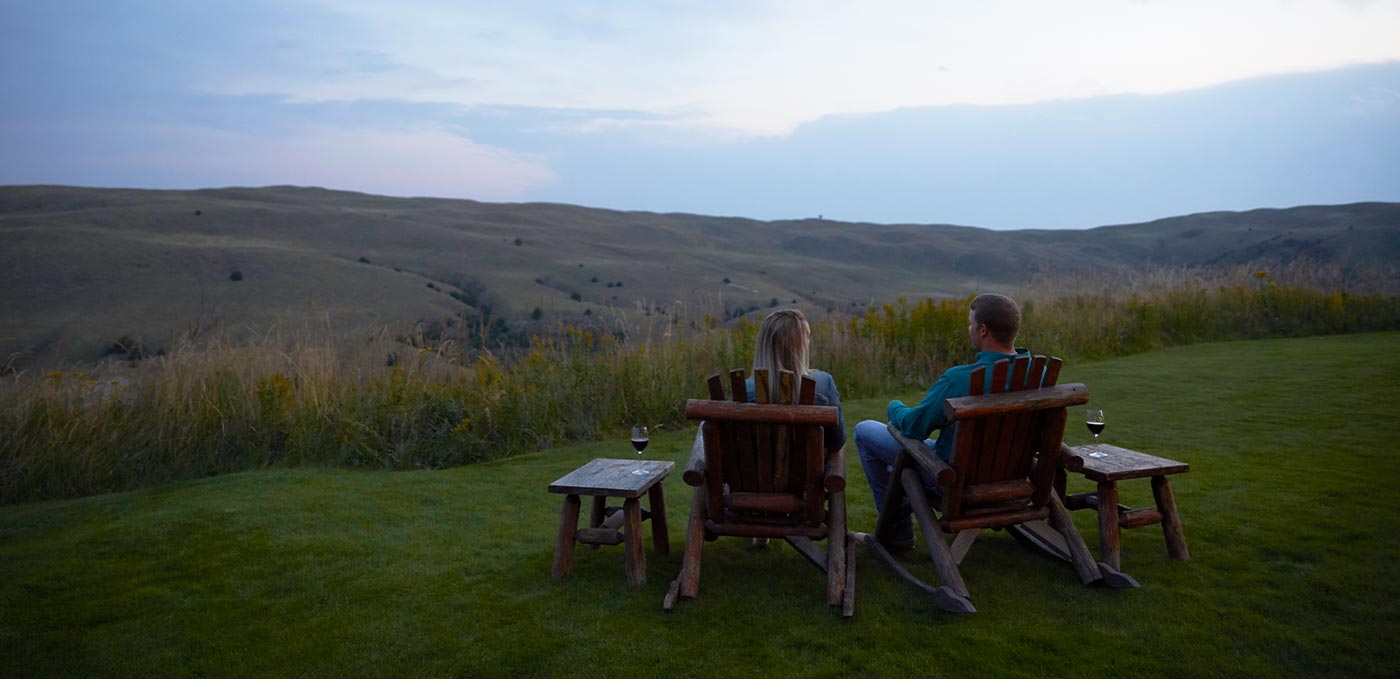 two people sitting in log chairs with wine overlooking a vista