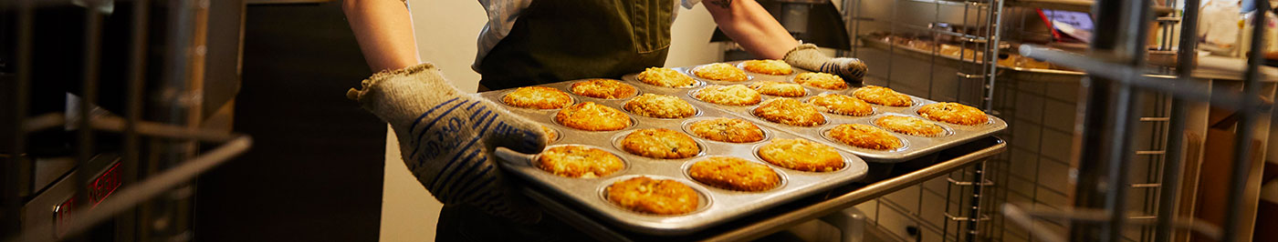 woman holding a pan of muffins at a bakery