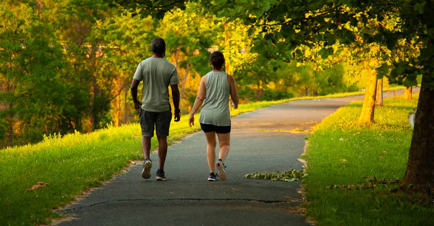 two people walking on paved hiking trail through park